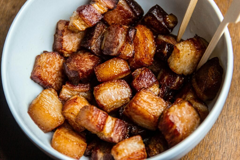 Close-up of crispy fried pork belly cubes served in a white bowl.